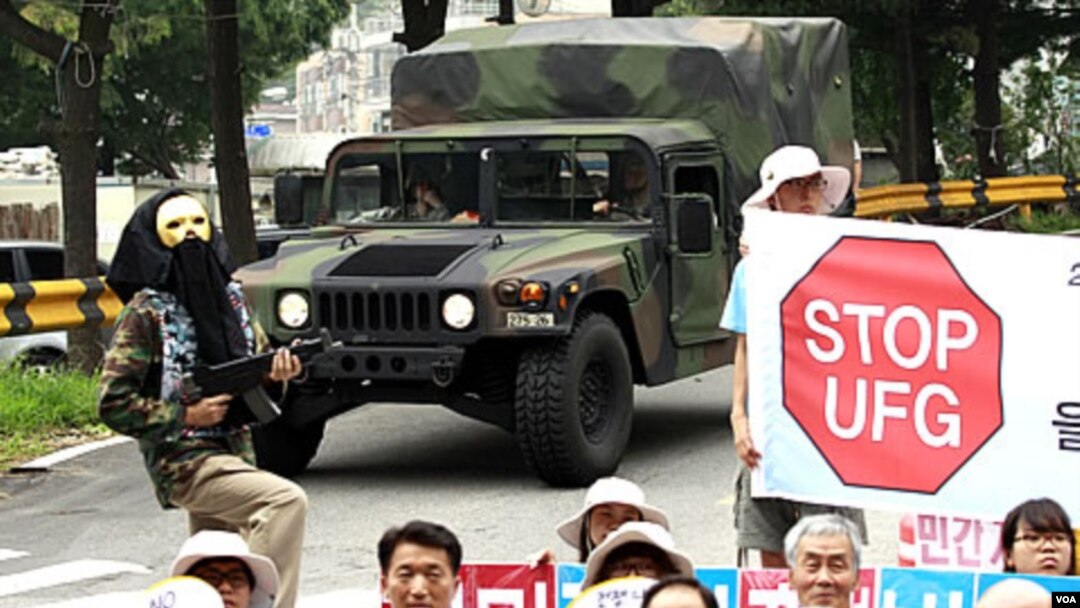Manifestantes reclaman en Corea del Sur contra los ejercicios militares, mientras un vehículo militar estadounidense pasa frente al grupo.