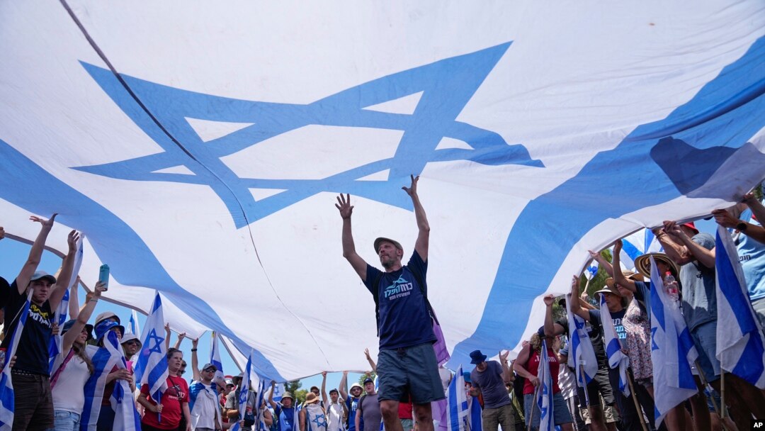 Manifestantes ondean una gran bandera israelí durante una protesta contra los planes del gobierno del primer ministro Benjamin Netanyahu para reformar el sistema judicial, frente a la Knesset, el parlamento de Israel, en Jerusalén, el lunes 24 de julio de 2023.