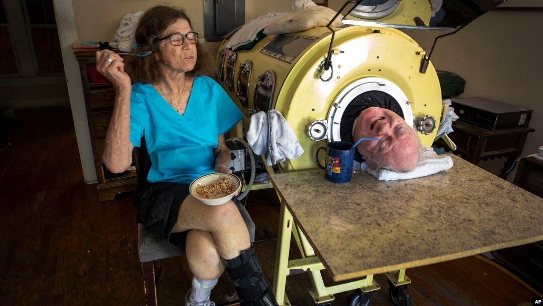 ARCHIVO - En esta fotografía del viernes 27 de abril de 2018, el abogado Paul Alexander conversa con su cuidadora y amiga Kathryn Gaines mientras él toma café y ella desayuna junto a su pulmón de hierro en su casa en Dallas.