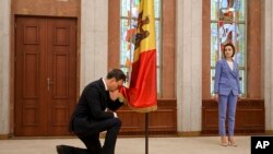 Moldova's president Maia Sandu, right, watches as Moldovan Prime Minister Dorin Recean kneels down in front of the national flag during a swearing-in ceremony in Chisinau, Feb. 16, 2023.