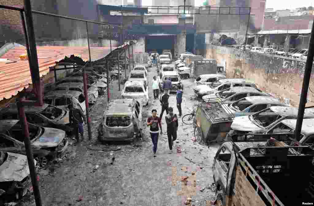 Men look at burnt vehicles at a parking lot following clashes between people demonstrating for and against a new citizenship law in New Delhi, India.