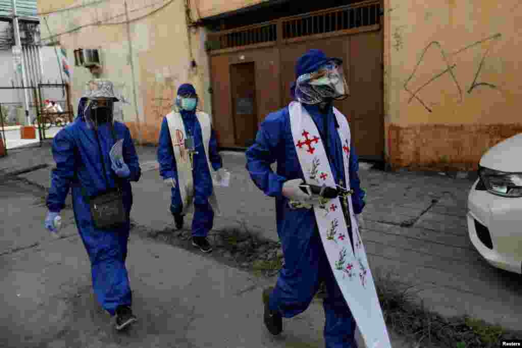 Filipino Catholic priests Eduardo "Ponpon" Vasquez Jr. and Rey Amancio, wearing personal protective equipment, make their way to a home to bless a deceased woman's ashes, amid the prohibition of religious gatherings, including funerals, during the lockdown to contain the coronavirus outbreak, in Caloocan, Metro Manila, Philippines. 