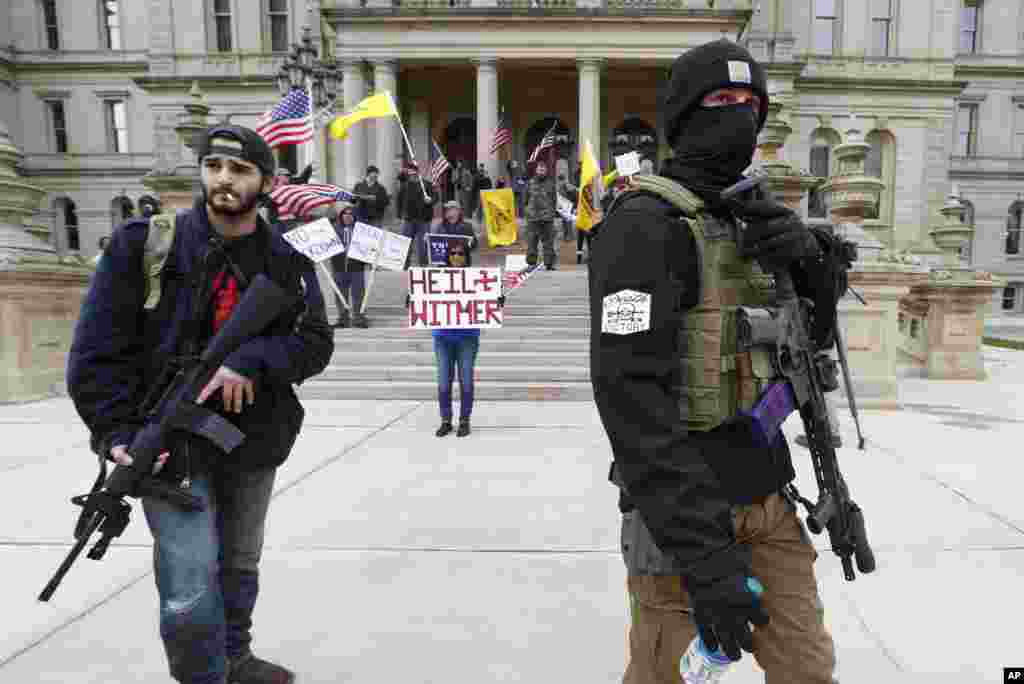 Protesters carry rifles near the steps of the Michigan State Capitol building in Lansing, Michigan, April 15, 2020. Flag-waving, honking protesters drove past the Michigan Capitol to show their displeasure with Gov. Gretchen Whitmer's orders to keep people at home and businesses locked during the coronavirus outbreak.