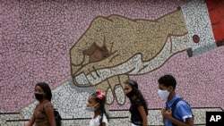 Jóvenes con mascarillas pasan frente a un mural de mosaico con la imagen de una mano depositando una boleta, en Caracas, Venezuela. Octubre 11, 2020.