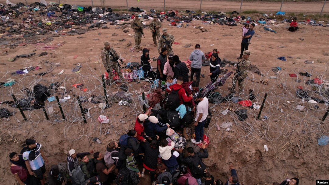 Migrantes intentan cruzar una valla de alambre de púas desplegada para impedir el cruce de migrantes a EEUU, a orillas del río Bravo, en la frontera con México, visto desde Piedras Negras, Coahuila, el 21 de diciembre de 2023.