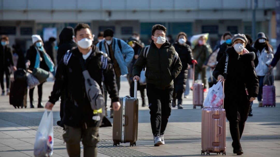 Travelers wear face masks as they walk outside the Beijing Railway Station in Beijing, Saturday, Feb. 15, 2020. (AP Photo/Mark Schiefelbein)