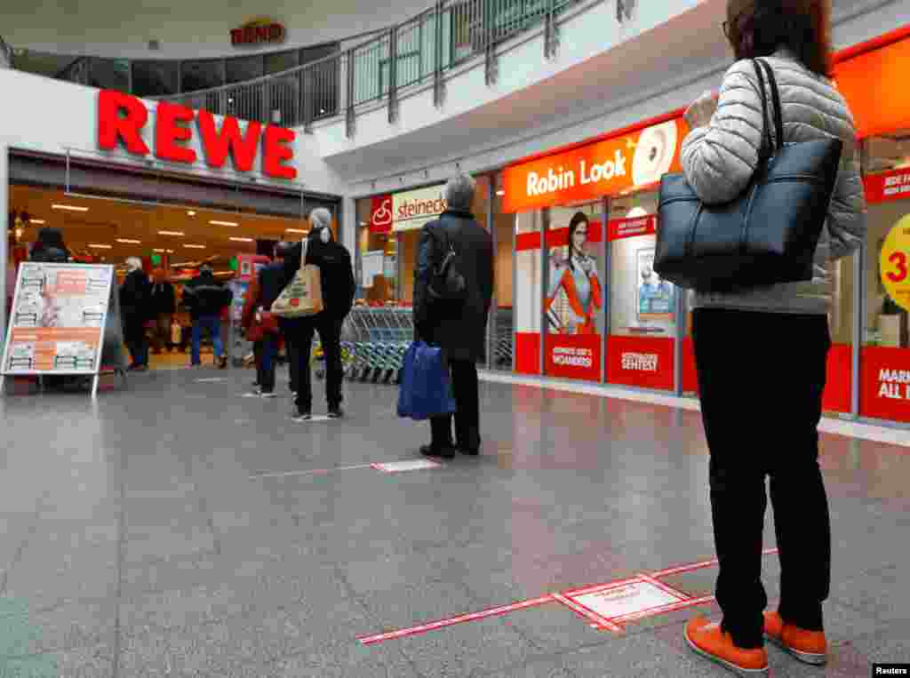 People wait to enter a shop, behind red lines that mark the distance customers have to keep between them, at a Rewe grocery store in Potsdam, Germany.