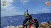 En esta imagen tomada de un video distribuido el domingo 6 de agosto de 2023 por miembros del equipo de Rescate Alpino Italiano, un migrante varado en un arrecife rocoso en la diminuta isla de Lampedusa es ascendido a un helicóptero de rescate. 