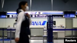 一名员工在冠状病毒爆发后戴着防护口罩，经过在日本大阪关西国际机场几乎全空的全日空柜台。（2020年3月14日）