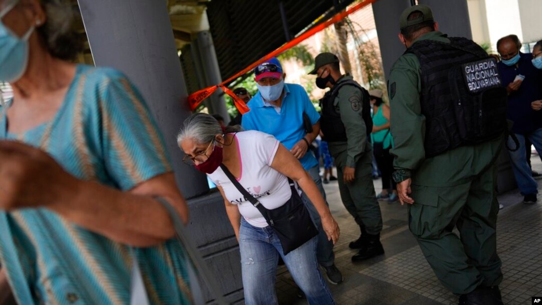 Los residentes pasan por debajo de una tira de cinta adhesiva que sirve como barrera mientras se dirigen a un área donde se les inyectará una segunda dosis de la vacuna Sputnik V COVID-19 en Caracas. Septiembre 21, 2021.