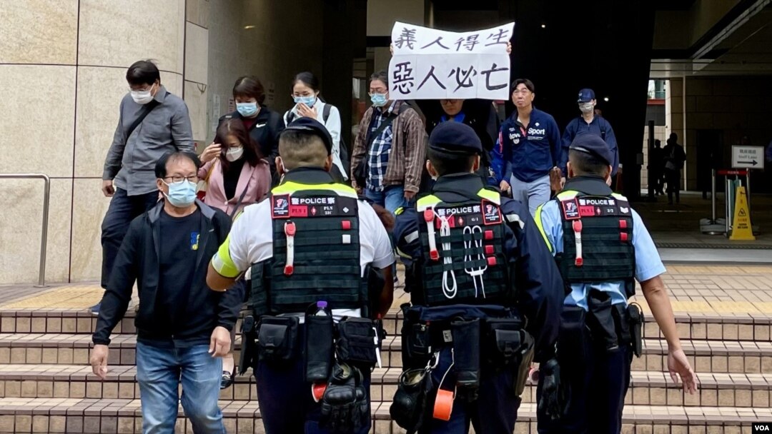 香港民主派初選案被告呂智恆的養母Elsa，判刑後在西九龍裁判法院大樓外高舉”義人得生、惡人必亡”的標語，她隨即被多名警員包圍及帶上警車。(美國之音照片)