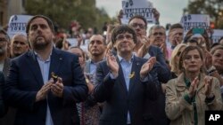 El vicepresidente catalán, Oriol Junqueras (izquierda), el presidente catalán, Carlos Puigdemont (segundo desde la izquierda) y Carne Forcadell, líder de la Cámara del Parlamento catalán aplauden durante una manifestación contra la decisión de Madrid el sábado, 21 de octubre de 2017.