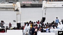 Activistas sostienen una pancarta que dice "Detengan el ataque a los refugiados" mientras los inmigrantes aguardan para desembarcar del buque "Disciotti" de la Guardia Costera italiana, en el puerto siciliano de Catania, en el sur de Italia, el miércoles 13 de junio de 2018.