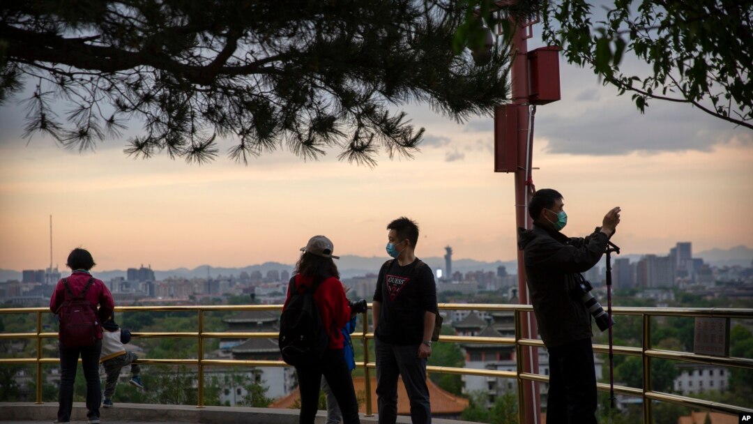 Varias personas con máscaras para protegerse del nuevo coronavirus observan el panorama desde un mirador en el tope de una colina en un parque público de Beijing, el sábado 25 de abril de 2020.