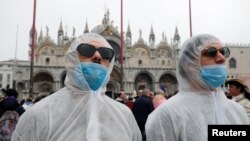 FILE - Tourists wear protective face masks at Venice Carnival, which the last two days of, as well as Sunday night's festivities, have been cancelled because of an outbreak of coronavirus, in Venice, Italy, Feb. 23, 2020. 